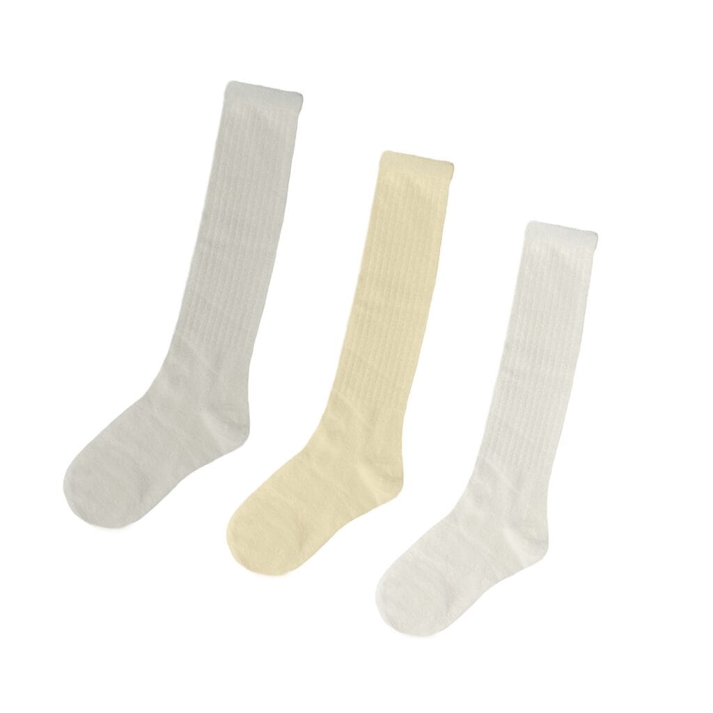 Three knee-high socks laid flat side by side in light grey, cream, and white, each made of ribbed fabric and displayed against a plain background.